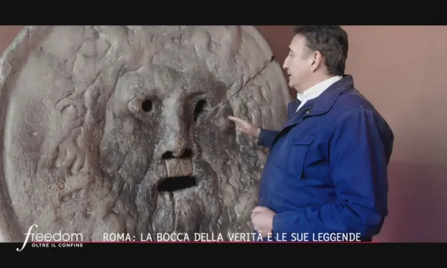 Un uomo indica la Bocca della Verità a Roma, un'antica scultura che si dice morda la mano dei bugiardi. Il suo significato è legato alla giustizia e alla verità.