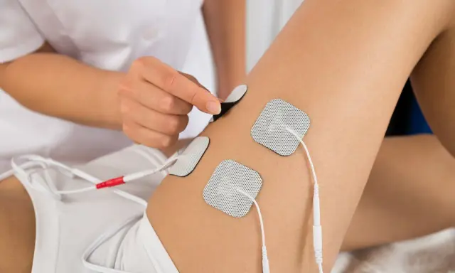 Terapeuta umieszcza elektrody na udzie pacjenta, przygotowując do zabiegu elektrostymulacji.