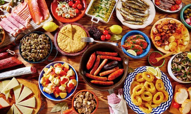 Tapas co to? Kolorowy stół pełen hiszpańskich przekąsek: kiełbaski, krewetki, owoce morza, tortilla, sery i wędliny. Prawdziwa uczta!
