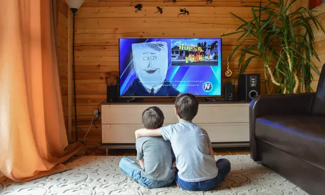 Dwóch chłopców ogląda bajkę w telewizji, która może być szkodliwa dla dzieci. Na ekranie postać z workiem na głowie i napis "HOUSE FIRE!".