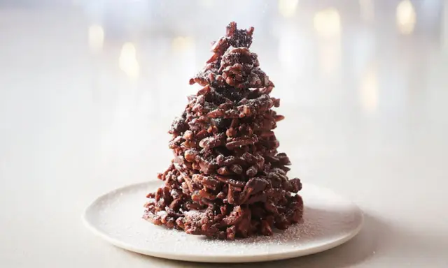 Un sapin chocolat mikado, saupoudré de sucre glace, sur une assiette blanche. Un délice festif !