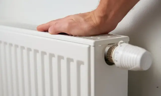 Mano tocando un radiador blanco, listo para cuando encender la calefacción. Termostato visible.
