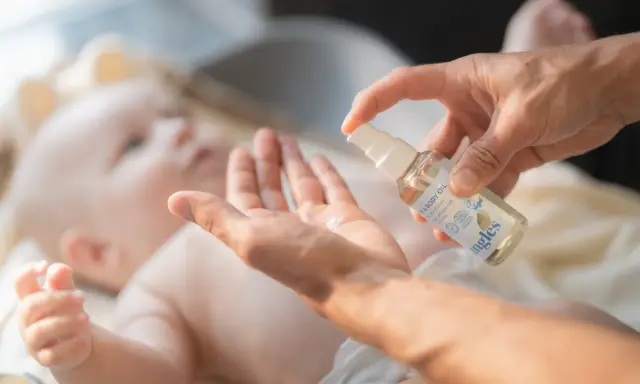 En hand sprutar olja i en annan hand, redo att smörja en bebis. Kanske för att lindra skorv bebis.