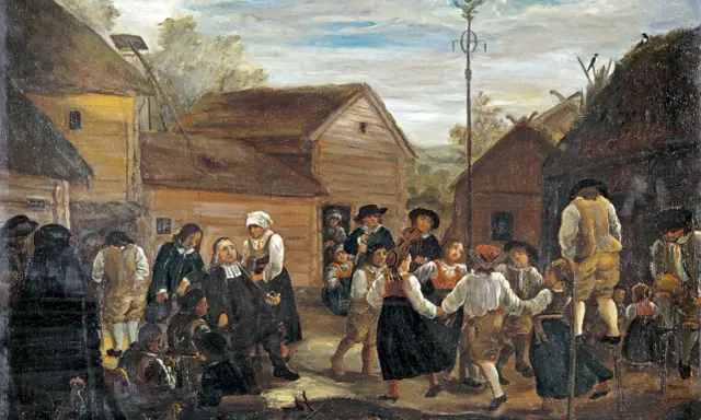 Midsommarhistoria: Människor i folkdräkter dansar runt en majstång i en by.