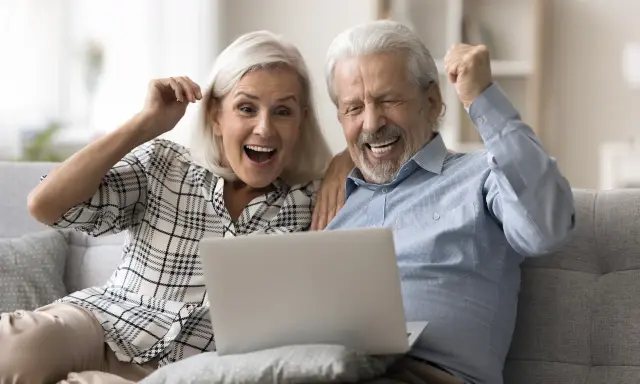 Szczęśliwi seniorzy sprawdzają na laptopie przeliczenie emerytury rocznik 1949 do 1953.