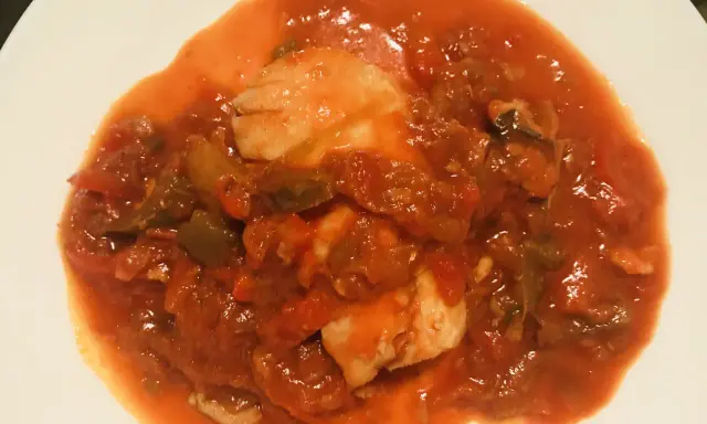 Un plato de urta a la roteña, con trozos de pescado blanco en una salsa roja de tomate y verduras.