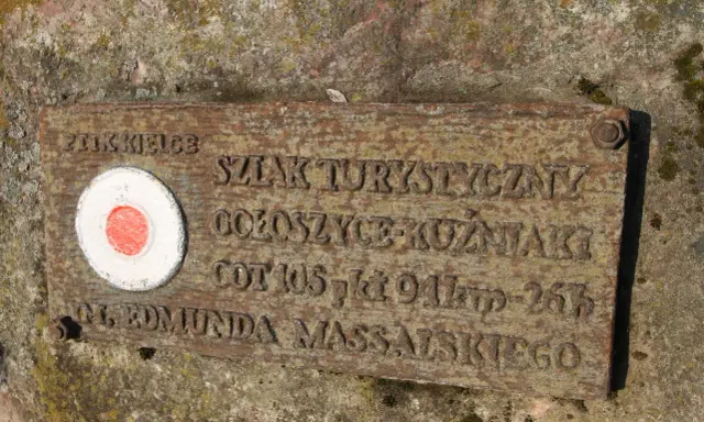 Tabliczka na skale z czerwono-białym kołem i napisem "Główny szlak świętokrzyski im. Edmunda Massalskiego".