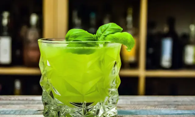 Orzeźwiający drink z likierem miętowym, ozdobiony listkami bazylii, w szklance o geometrycznym kształcie.