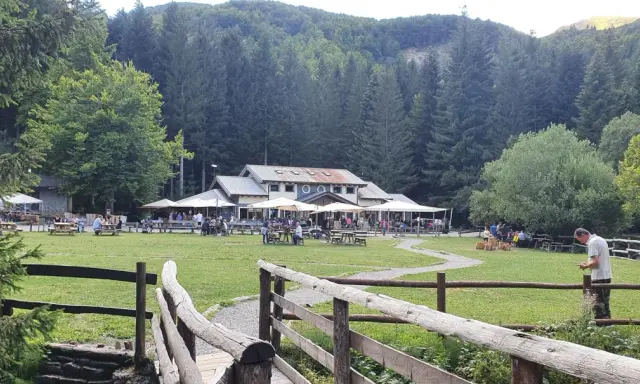 Un rifugio in Emilia Romagna immerso nel verde, con tavoli all'aperto e persone che si godono la giornata.