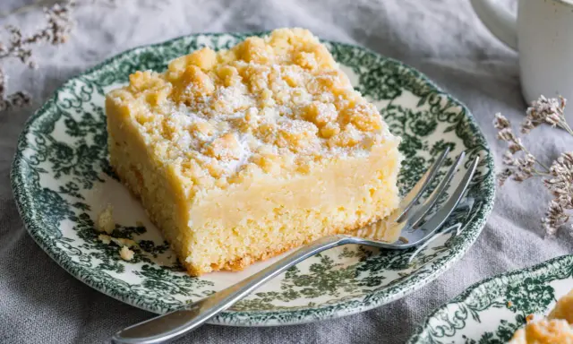 Ein Stück Streuselkuchen ohne Hefe, bestäubt mit Puderzucker, auf einem Teller mit grünem Muster.