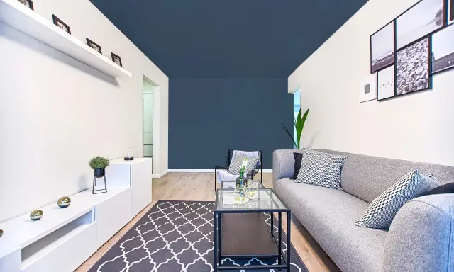 Un salon moderne avec un canapé gris, une table basse en verre et un tapis à motifs. Le plafond bleu foncé donne une impression de profondeur, une astuce pour comment agrandir une pièce.