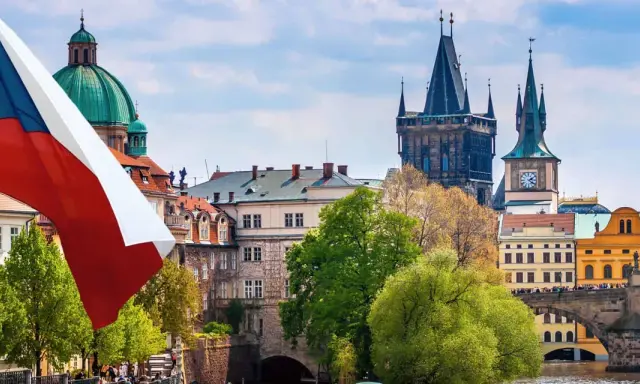 Flaga Czech powiewa nad Pragą, ukazując ciekawe fakty o Czechach. W tle widać Most Karola i wieże.