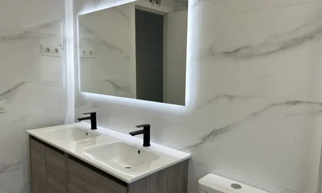 Moderno lavabo doble con grifería negra y espejo iluminado. Una solución ideal para reformar baño sin obras, con un toque de elegancia.
