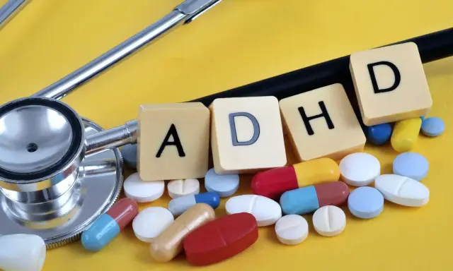 Stetoskop i tabletki symbolizujące leki na ADHD. Litery A, D, H, D ułożone na żółtym tle.