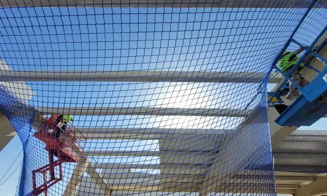 Trabajadores en plataformas elevadoras instalan una red de protección colectiva sobre una estructura en construcción, garantizando la seguridad.