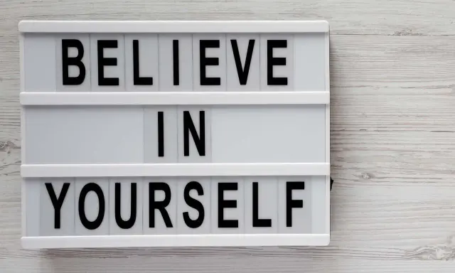 Biała tablica z czarnymi literami: "BELIEVE IN YOURSELF". To przesłanie inspiruje do nastawienia na rozwój i wiary we własne możliwości.