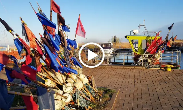 Stos kolorowych flag rybackich i bojki na nabrzeżu przy łodziach.