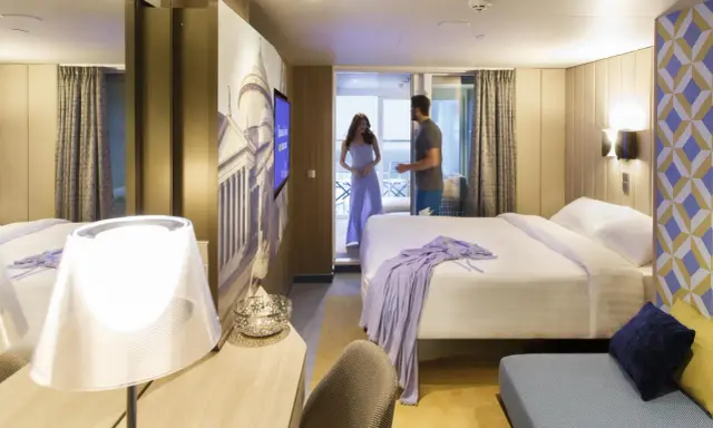 Coppia in una moderna cabina interna di Costa Crociere. Letto matrimoniale, decorazioni artistiche e un balcone invitano al relax.