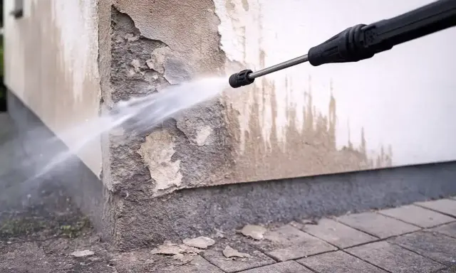 Hochdruckreiniger sprüht Wasser auf eine beschädigte Hauswand, um die Fassade zu reinigen.