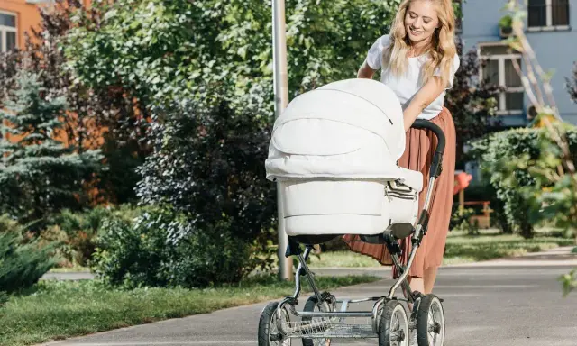 Uśmiechnięta mama spaceruje z białym wózkiem, który jest wyposażony w praktyczne akcesoria.