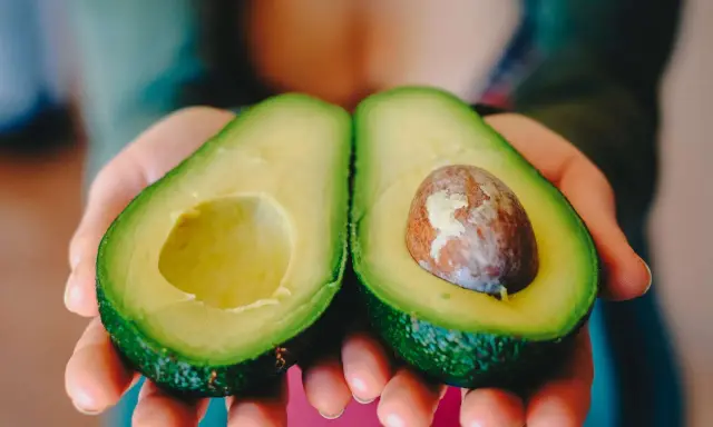 Zwei Hälften einer Avocado werden in Händen gehalten. Eine Hälfte hat den Kern, die andere ist leer. Perfekt, um die Avocado reifen zu lassen.