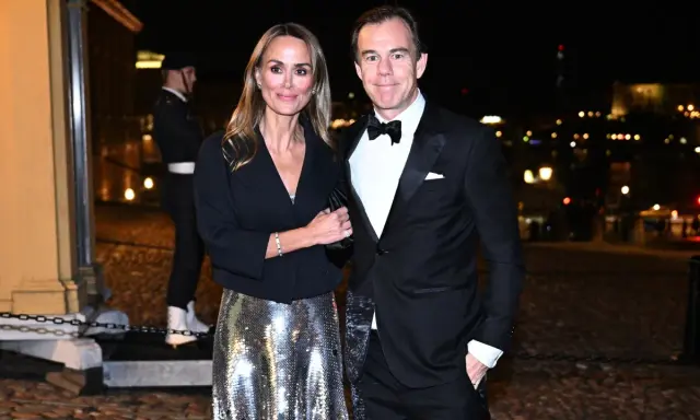 A couple in formal attire poses at night with a blurred city background.