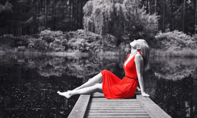 Mujer con vestido rojo sentada en muelle, efecto blanco y negro photoshop.