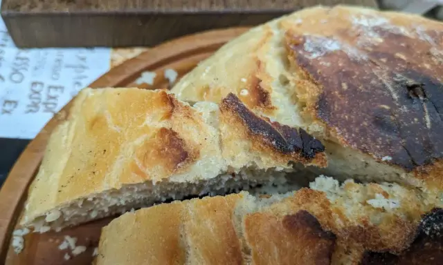 Ein knuspriges, goldbraunes dutch oven brot mit einer luftigen Krume, auf einem Holzbrett serviert.