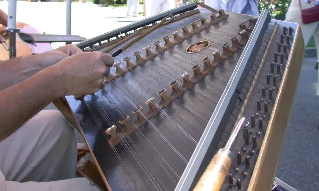 Dłonie grają na cymbałach, instrumencie strunowym, w słoneczny dzień.