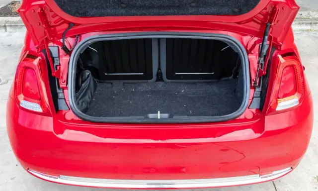 Maletero abierto de un Fiat 500 rojo, mostrando el espacio de carga cubierto de fieltro oscuro.