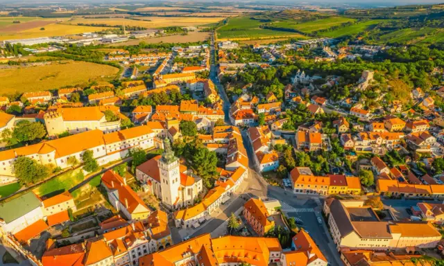 Malownicze miasteczko na Morawach w Czechach, z dominującą wieżą kościelną i pomarańczowymi dachami, otoczone zielonymi wzgórzami.