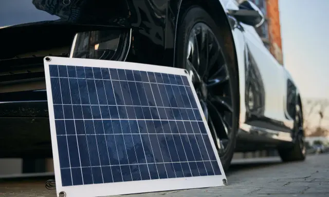 Panel solar portátil junto a un coche eléctrico, listo para cargar en casa.