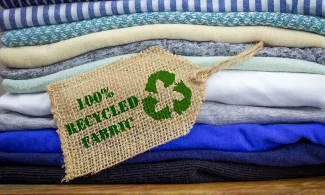 Pile di tessuti ecologici colorati, con un'etichetta che indica "100% Recycled Fabric" e il simbolo del riciclo.