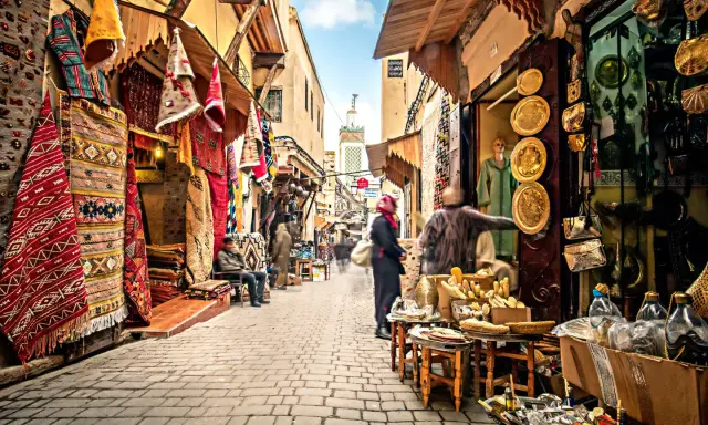 Bunte Teppiche und Souvenirs säumen einen belebten suk markt. Menschen schlendern durch die Gasse, vorbei an Geschäften voller Schätze.