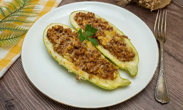 Dos mitades de calabacines rellenos de carne picada y queso gratinado, decorados con perejil. Un plato casero y delicioso.