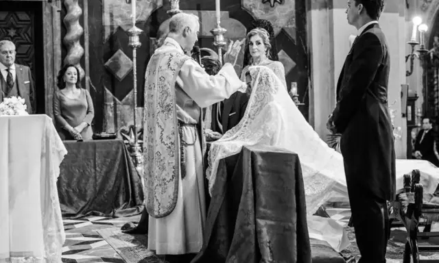 Sacerdote bendice a la pareja durante el rito de la velación. Novia con velo, novio de etiqueta, invitados y altar en iglesia.