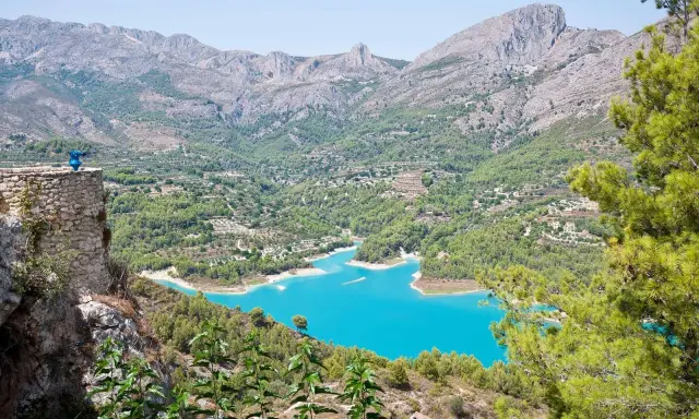 Espectacular vista de la ruta pueblos interior Alicante, con un embalse turquesa rodeado de montañas y vegetación.
