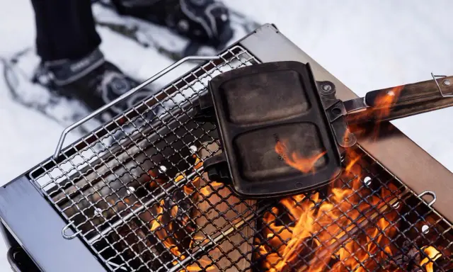 En smörgåsgrill värms över en eld, perfekt för friluftsmat recept i snön.