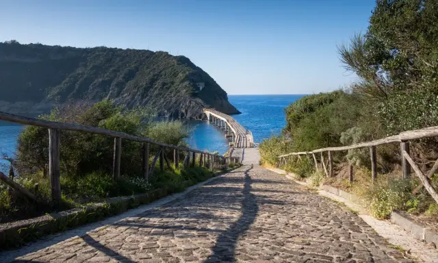 Sentiero acciottolato verso un ponte sul mare, ideale per cammini in Italia sul mare.