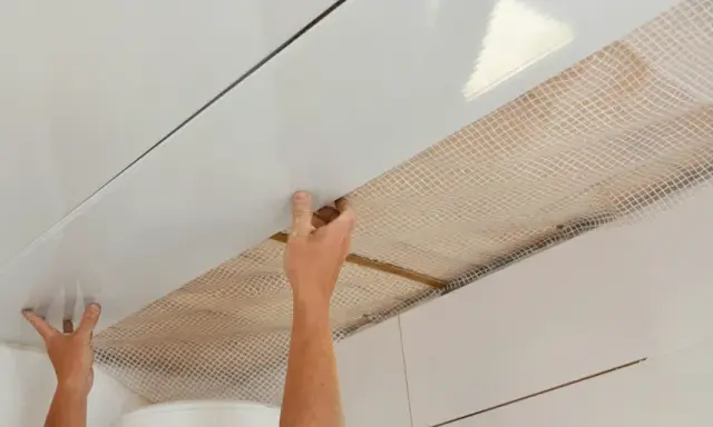 Mains installant des panneaux blancs pour refaire un plafond, avec un treillis visible en dessous.
