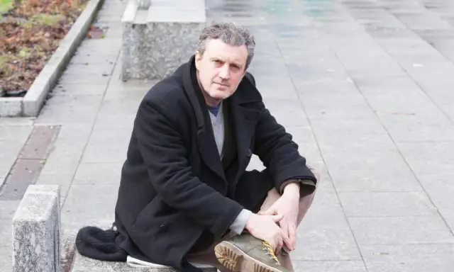 Uomo con cappotto nero seduto all'aperto, ricorda le atmosfere dei rocco schiavone libri.