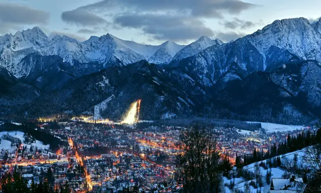 Oświetlone miasto Zakopane nocą, otoczone ośnieżonymi górami. Idealne miejsce na zakup biletów na zimowy wypoczynek.