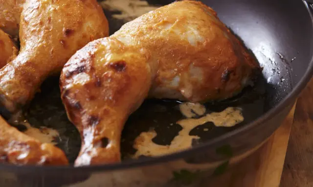 Cosce di pollo dorate e succulente cuociono in padella, emanando un profumo invitante.