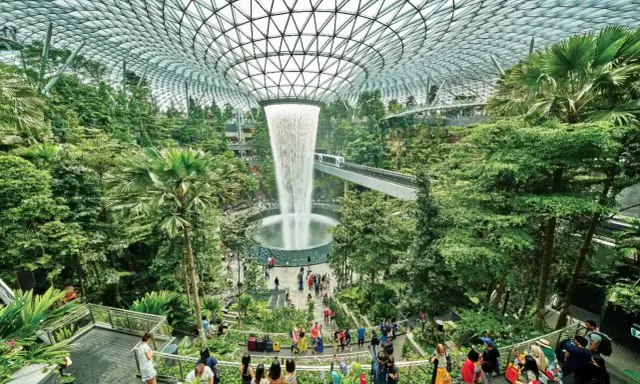Imponerande vattenfall och frodig grönska under glastaket på singapore flygplats. Människor njuter av den unika miljön.