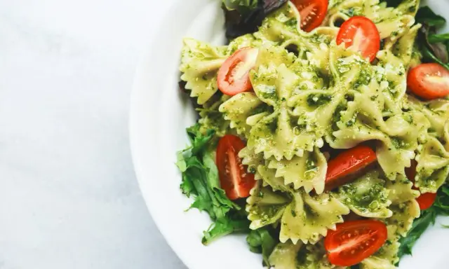 Pyszny makaron z pesto, udekorowany pomidorkami koktajlowymi i świeżą sałatą, podany na białym talerzu.