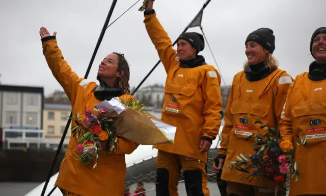 Des femmes en cirés jaunes célèbrent la fin du célèbre projet, bouquets à la main.