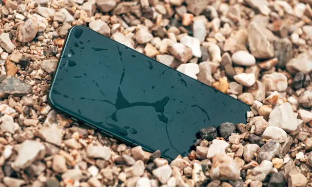 Smartfon leży na kamieniach, mokry, ale wytrzymały zgodnie ze **standardem militarnym MIL-STD-810H**.