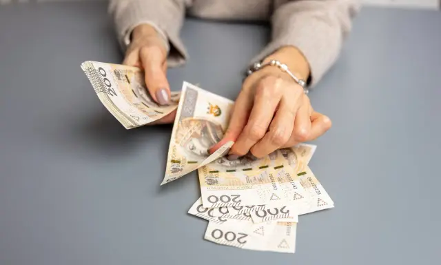 Dłonie liczą banknoty 200 zł. To może być wypłata świadczenia urlopowego na wymarzone wakacje.