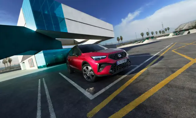 Czerwony Seat Arona, jeden z najnowszych seat modele, zaparkowany przy nowoczesnym budynku z niebieskimi akcentami.