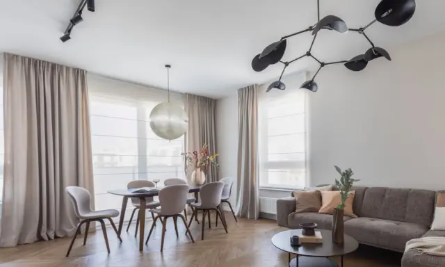 Nowoczesne oświetlenie salonu z jadalnią: designerski żyrandol i reflektory nad stołem. Aranżacje wnętrz z klasą.